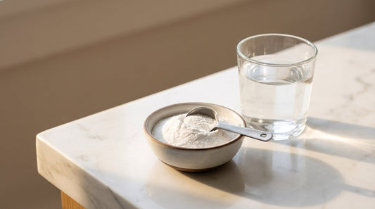 Creatine monohydrate powder in ceramic bowl with measuring scoop on white marble